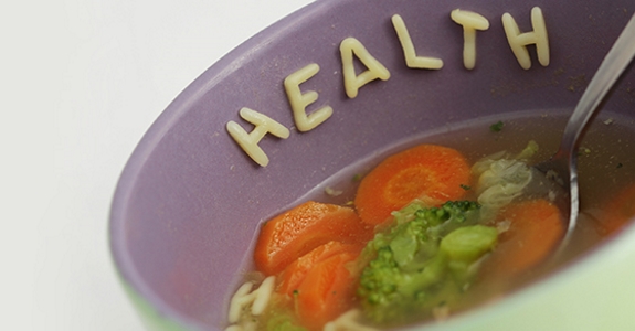 Eating healthy with vegetable soup, noodle letters forming 'health'