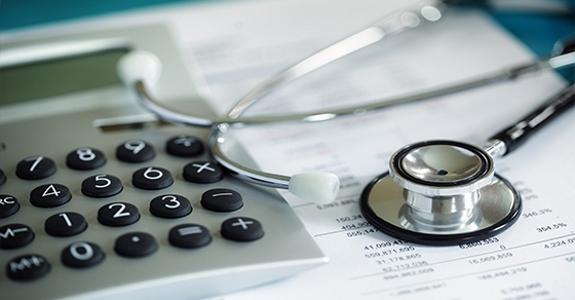 Photo of calculator and stethoscope on top of financial statement