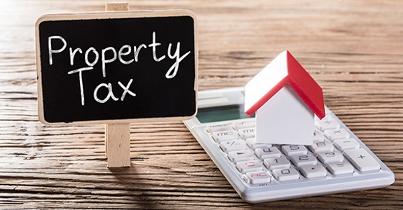 Picture of pocket calculator with toy house on top of it next to "Property Tax" sign