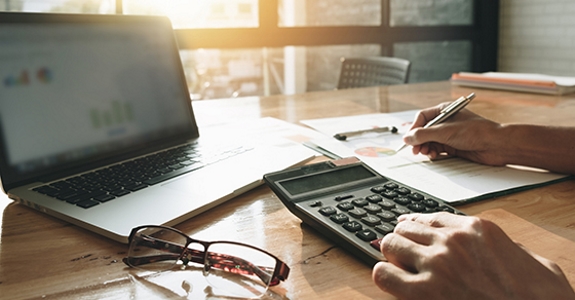 Laptop, calculator, eyeglasses, and notebook on desk