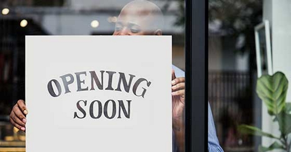 Man holding "Opening Soon" sign behind window