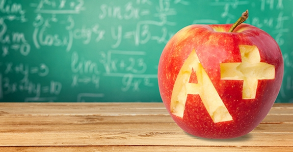 Apple with A+ carved into it on table in front of chalkboard