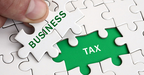 Hand placing puzzle pieces labeled "BUSINESS" on a platform labeled "TAX"
