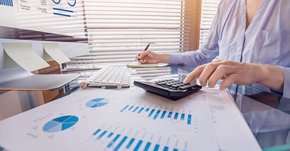 Person using a calculator, a computer, and graphs.