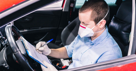 Man in car, wearing PPE and writing on a clipboard