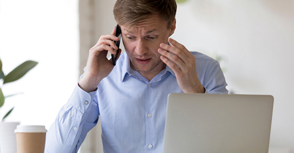 Overwhelmed businessperson sitting at desk and talking on phone