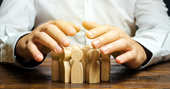 Photo of hands trying to contain a group of wooden figures on a table
