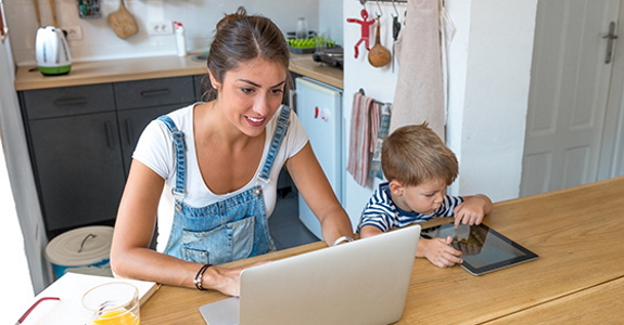 Woman using laptop next to child in kitchen