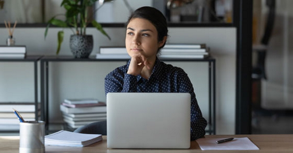 Woman looking off to the distance while sitting at laptop